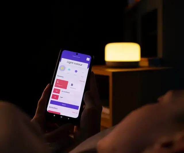 Persona en penumbra buscando alojamiento en el celular, con una lámpara encendida de fondo