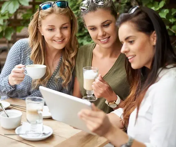 Tres amigas en un café mirando reseñas en una tablet